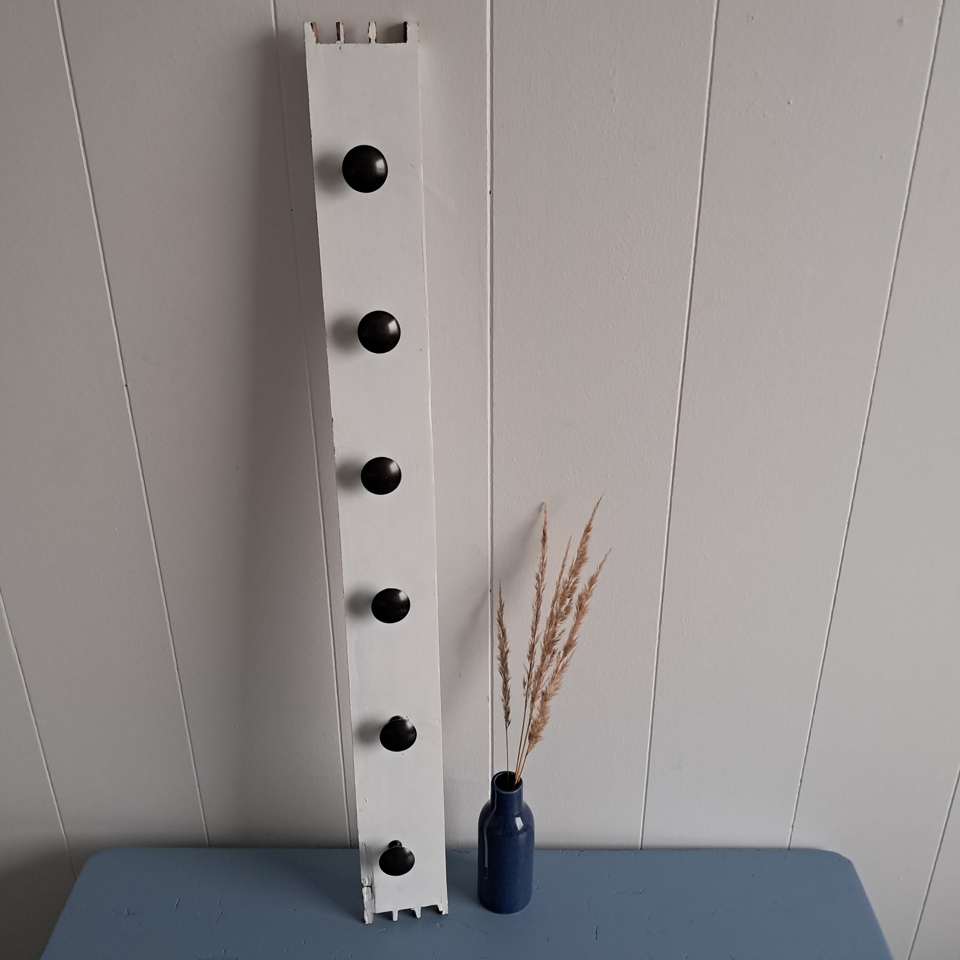 Knagerække med 6 sorte greb, hvid baggrund, blå vase med tørrede blomster